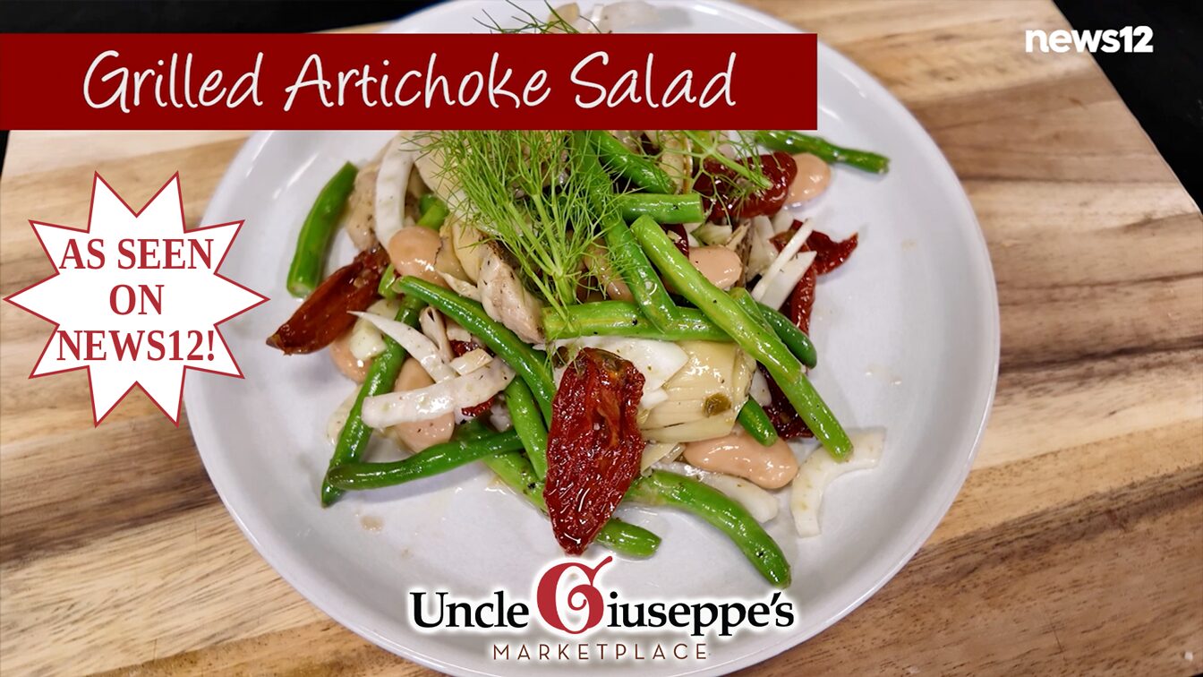 grilled artichoke salad on a white plate resting on a wood cutting board