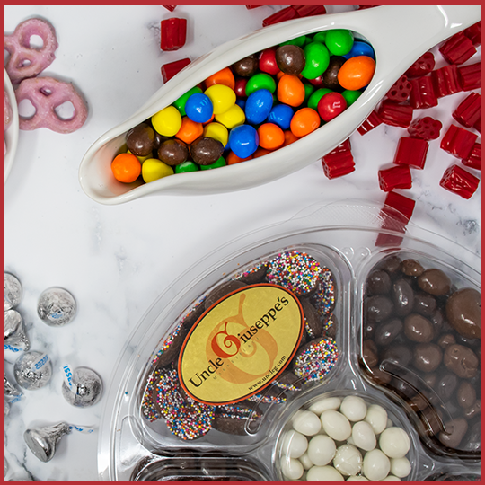 Gravy boat filled with m&ms and Uncle Giuseppe's candy platter on a white background with candy scattered