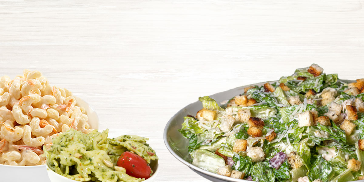 White wood background with macaroni salad, pesto salad and caesar salad on it